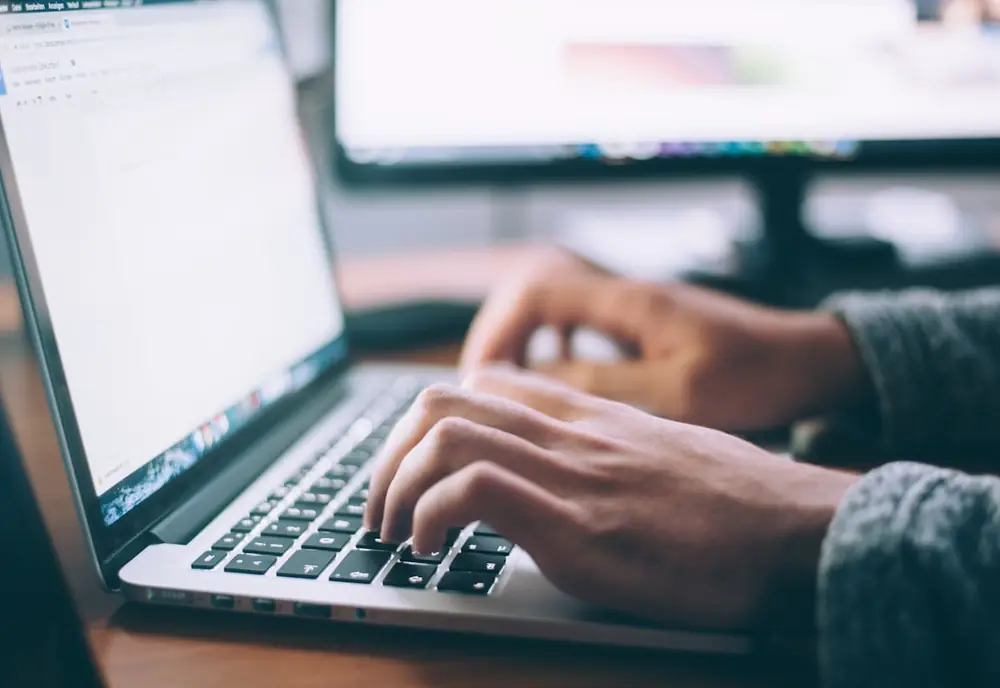 Manos escribiendo en el teclado de un portátil con una página web abierta