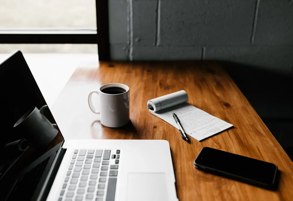 Mesa de trabajo con un portátil, una libreta y una taza de café